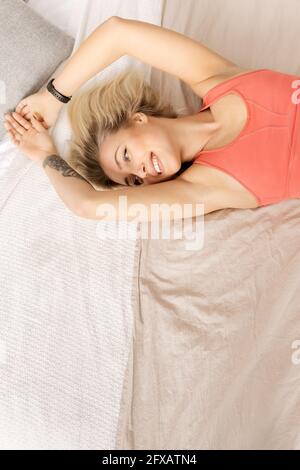 Jeune fille blonde se réveillant, regardant le côté, souriant. Belle femme de bonne humeur se trouve sur le lit, s'étirant, se reposant après le matin Banque D'Images