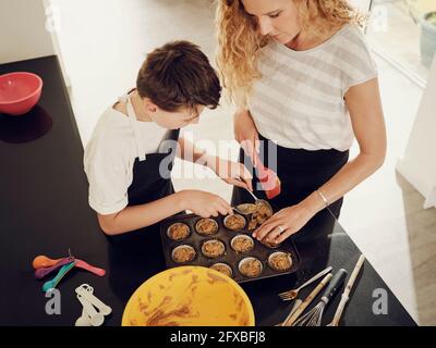 Mère enseignant à son fils de remplir le plateau à muffins de pâte dans la cuisine Banque D'Images