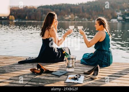 Les femmes organisateurs d'événements toaster le champagne tout en étant assis sur la jetée au-dessus du lac Banque D'Images