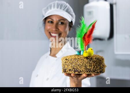 Chef féminin tenant un gâteau avec des plumes dans la cuisine Banque D'Images