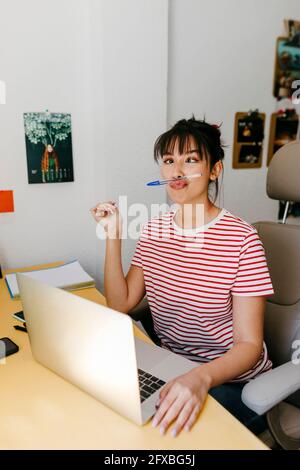 Femme faisant un visage en jouant avec le stylo à la maison Banque D'Images