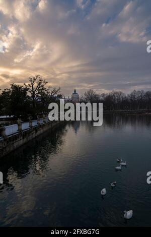 Vue sur les jardins au coucher du soleil et un bâtiment en arrière-plan depuis un pont au-dessus de la rivière avec des canards nageant, un après-midi d'hiver fraîchement enneigé Banque D'Images