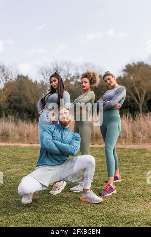 Des amies debout derrière un jeune homme qui s'accroupette dans le parc Banque D'Images