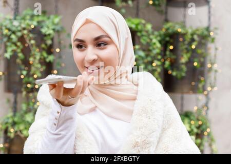 Jeune femme portant le hijab parlant sur un smartphone par le biais d'un haut-parleur Banque D'Images