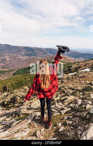 Femme avec le bras levé tenant le chapeau sur la montagne Banque D'Images