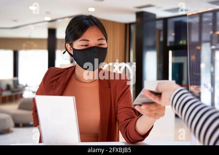 Une jeune femme sous masque prend la clé de la réceptionniste de l'hôtel Banque D'Images