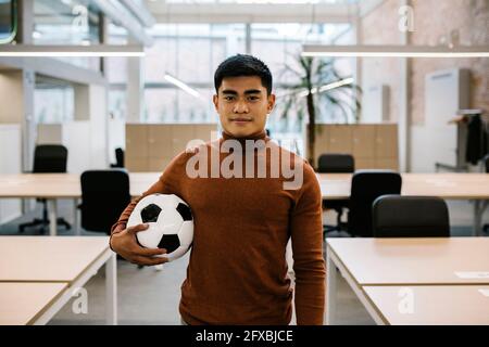 Beau homme d'affaires tenant le ballon de football au bureau Banque D'Images