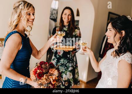 Bonne mariée avec des amies qui boivent du vin dans la chambre familiale Banque D'Images