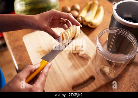 Femme coupant la banane sur une planche en bois dans la cuisine Banque D'Images