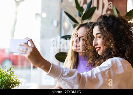 Des amies multiethniques emportant un selfie sur un téléphone portable dans un restaurant Banque D'Images