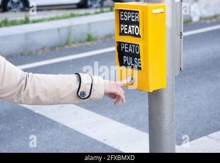 Doigt de femme appuyant sur le bouton piéton d'un feu de circulation. Les mots qui apparaissent signifient : « attendre piéton », « appuyer piéton ». Banque D'Images