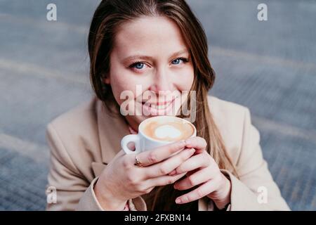 Femme souriante avec une tasse de café au café-terrasse Banque D'Images