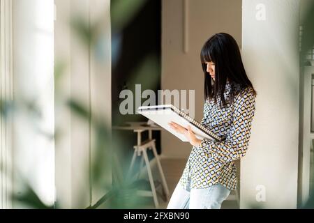 Femme entrepreneur tenant un carnet tout en se penchant sur la colonne Banque D'Images