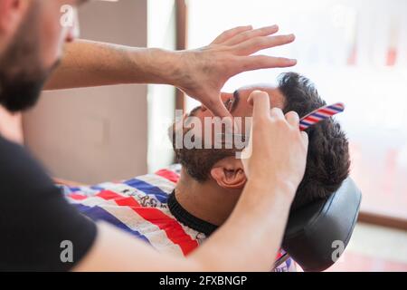 Coiffeur masculin taille de la barbe de l'homme avec un rasoir au salon Banque D'Images