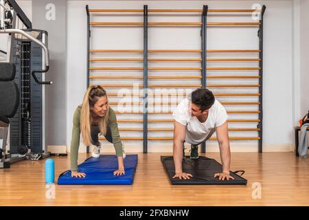Des athlètes souriants, hommes et femmes, font des push-up sur un tapis d'exercice dans la salle de gym Banque D'Images