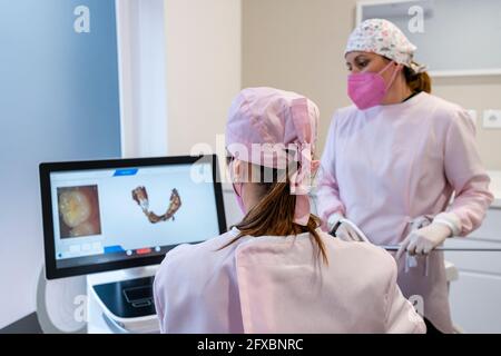 Les dentistes qui portent une coiffe chirurgicale examinent l'image numérique des dents à l'écran à la clinique Banque D'Images