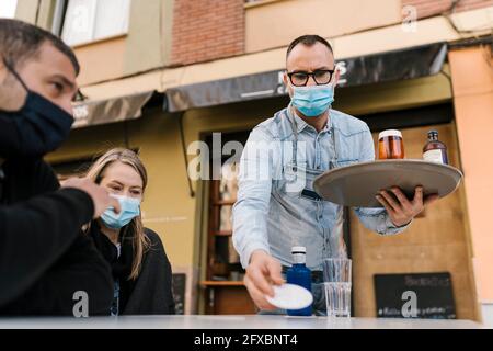 Serveur servant des boissons aux clients à l'extérieur d'un bar pendant une pandémie Banque D'Images