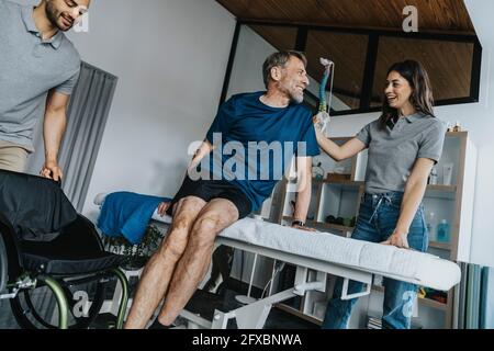 Femme en souriant physiothérapeute consolant le patient mâle mûr à la table de massage en pratique Banque D'Images