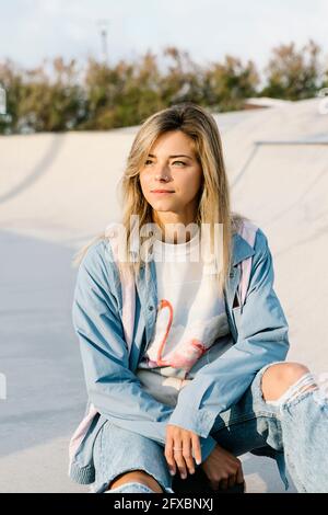 Belle femme regardant loin en s'asseyant dans le parc de skateboard Banque D'Images