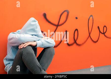 Un jeune garçon triste assis devant le mot allemand pour l'amour sur le mur orange Banque D'Images