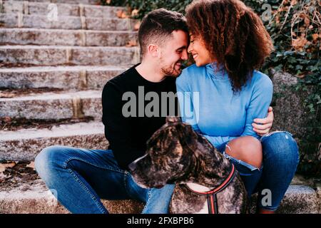 Couple souriant assis face à face sur les marches avec le chien American Pit Bull Terrier Banque D'Images