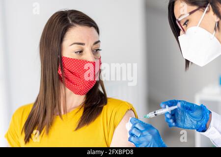 Femme portant un masque facial de protection regardant la femme médecin donnant le vaccin pendant COVID-19 Banque D'Images