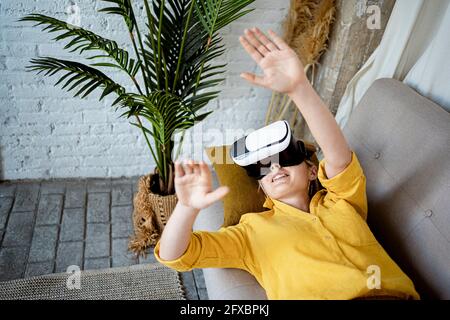 Jeune femme en gestuelle portant un simulateur de réalité virtuelle tout en étant allongé sur un canapé à la maison Banque D'Images