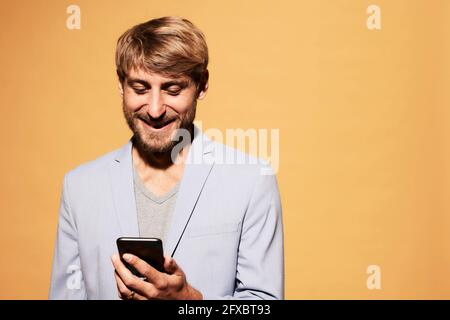 Homme souriant utilisant un smartphone devant un mur jaune Banque D'Images