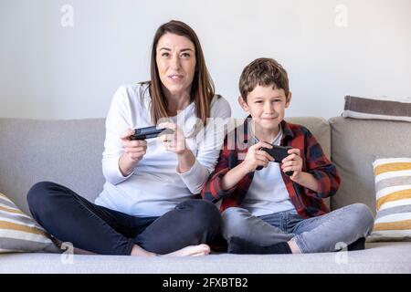 Femme et fils enthousiastes jouant à un jeu vidéo tout en étant assis sur un canapé dans le salon Banque D'Images
