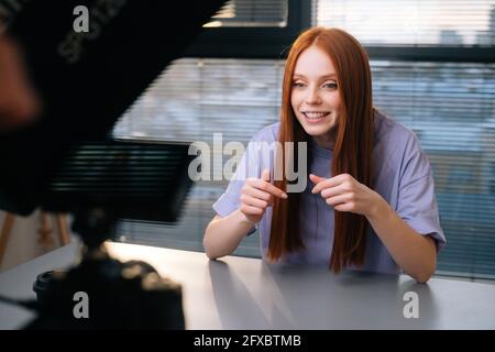 POV de gaie jeune femme blogger saluant les suiveurs pendant l'appel vidéo assis au bureau sur le fond de la fenêtre. Banque D'Images