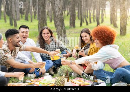 Des amis hommes et femmes joyeux qui profitent d'une fête pour pique-niquer dans la forêt Banque D'Images