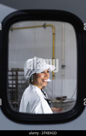 Femme souriante qui regarde loin de la cuisine vue dans le miroir Banque D'Images