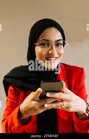 Femme souriante portant le hijab tenant le téléphone portable au café Banque D'Images