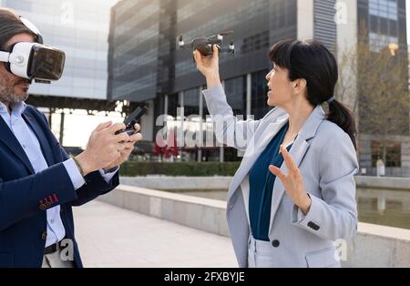 Homme d'affaires portant un casque de réalité virtuelle utilisant un drone à distance tout en se tenant debout avec une collègue dans le parc de bureau Banque D'Images