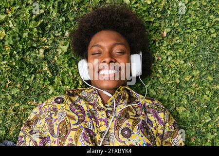 Femme souriante écoutant de la musique à l'aide d'un casque tout en étant allongée sur l'herbe Banque D'Images