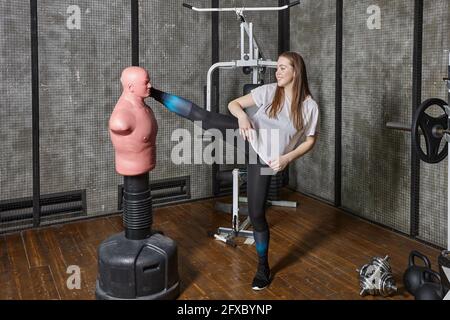 Bob ou sac de corps d'adversaire en salle de sport, jeune femme pratiquant des coups de pied. Banque D'Images