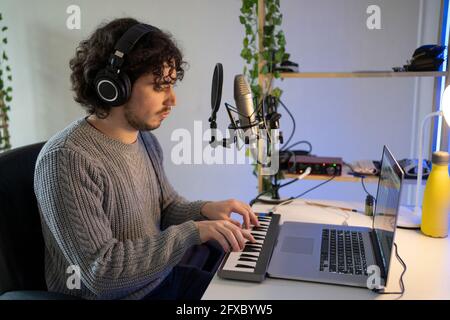 Musicien de sexe masculin avec un casque jouant du piano électrique à la maison Banque D'Images