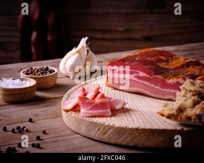 Bacon sur planche de bois avec sel et poivre dans des bols, ail et morceau de pain Banque D'Images