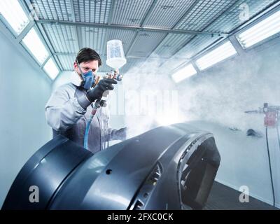 Peinture en aérosol mâle portant un masque facial de protection à l'aide d'un aérographe sur la partie du véhicule à l'atelier Banque D'Images