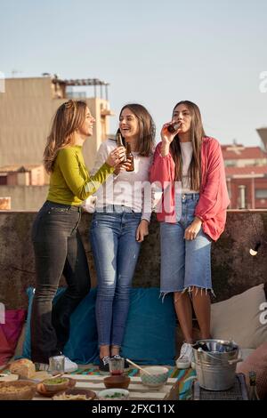 Des amies gaies buvant de la bière sur le toit Banque D'Images