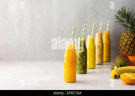 Smoothies aux fruits en pots avec pailles, ananas et kiwis sur les côtés, banane et mangue avec orange Banque D'Images