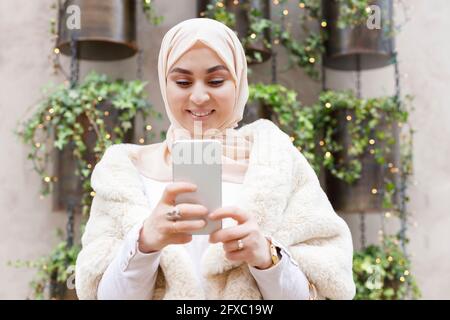 Femme souriante portant le hijab à l'aide d'un téléphone portable Banque D'Images