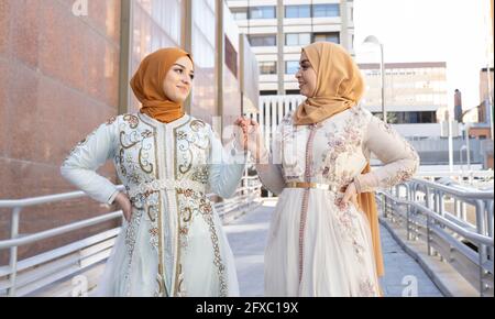 Les amis portant le hijab et s'habillent en souriant tout en tenant les mains sur le pont Banque D'Images