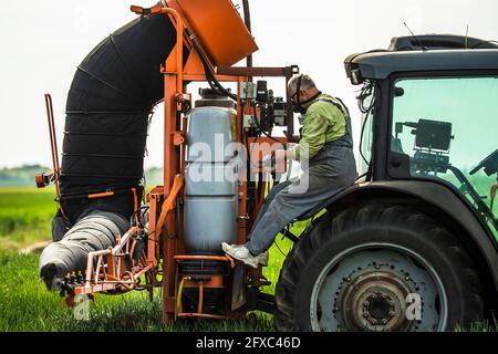 Un agriculteur mûr portant un masque de protection vérifie le conteneur de pesticides dans le tracteur Banque D'Images