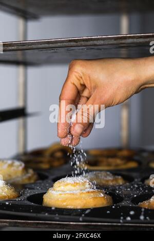 Saupoudrer à la main le sucre sur un petit pain à la cannelle dans la cuisine Banque D'Images