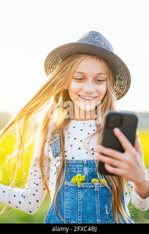 Une fille heureuse qui prend le selfie à travers un téléphone intelligent dans un champ agricole Banque D'Images