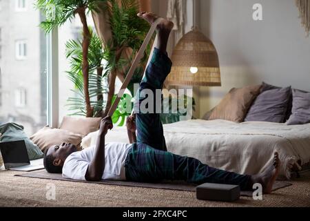 Jeune homme africain sportif travaillant à la maison, se réchauffant à l'aide de la ceinture yogique Banque D'Images