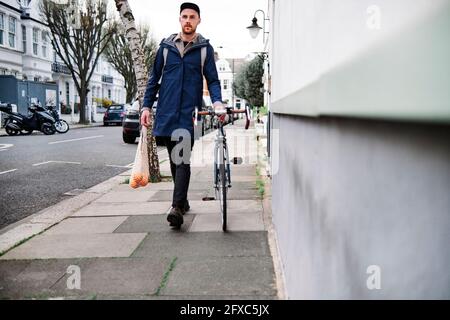 Jeune homme qui se labourant à vélo tout en tenant une sacoche d'oranges sur la piste de marche de la rue Banque D'Images