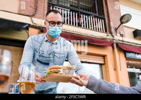 Un serveur sert des hamburgers et des frites au client assis à l'extérieur du bar pendant une pandémie Banque D'Images