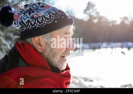 Homme senior avec écharpe rouge et chapeau tricoté pendant la journée ensoleillée en hiver Banque D'Images